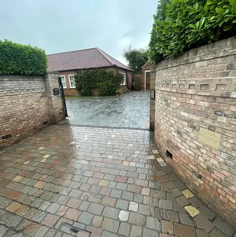 Newly installed cobblestone driveway entrance with brick wall pillars and lush hedge landscaping